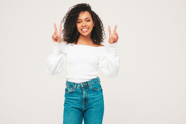 Hermosa mujer negra con peinado afro rizos. Modelo sonriente en suéter y ropa de jeans de moda