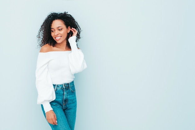 Hermosa mujer negra con peinado afro rizos. Modelo sonriente en suéter y ropa de jeans de moda