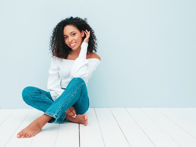 Hermosa mujer negra con peinado afro rizos. Modelo sonriente en suéter y ropa de jeans de moda