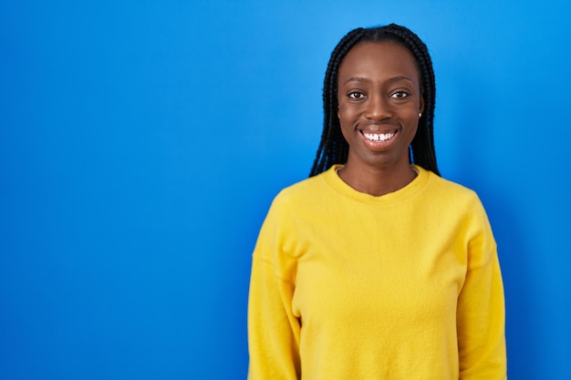 Hermosa mujer negra de pie sobre fondo azul con una sonrisa feliz y fresca en la cara. persona con suerte.