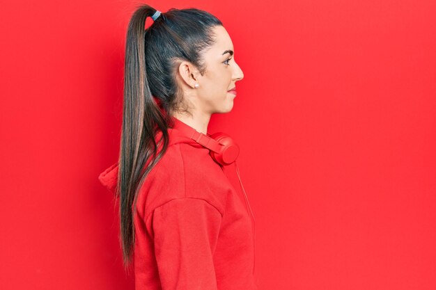 Hermosa mujer con ojos azules usando ropa de gimnasia y auriculares mirando hacia un lado, relaja la pose de perfil con rostro natural con una sonrisa segura.