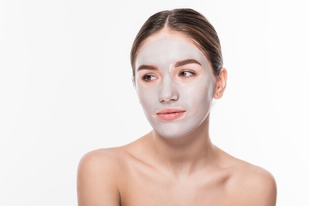 Hermosa mujer con los ojos cerrados y la máscara facial de arcilla blanca en la cara en la pared blanca