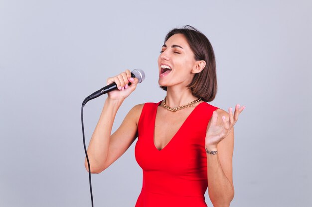 Hermosa mujer en pared gris con micrófono cantando canción favorita emocional feliz positivo alegre