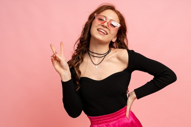 Foto gratuita hermosa mujer pelirroja en suglasses posando sobre pared rosa. pelos ondulados. sonrisa perfecta.