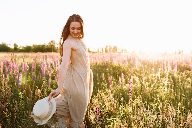 Hermosa mujer de pelo oscuro en un vestido de verano en un campo de flores florecientes de lupino