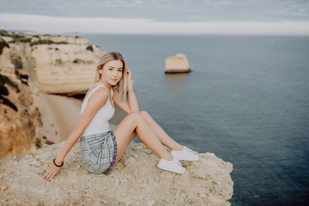 Hermosa mujer pensante sentada en la piedra en el océano azul