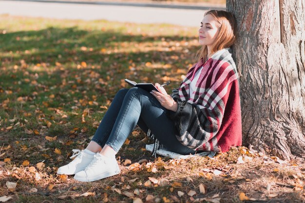 Hermosa mujer de pie cerca de un árbol de tiro largo