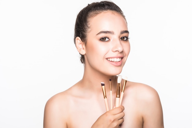 Hermosa mujer con pinceles de maquillaje cerca de su rostro aislado en la pared blanca