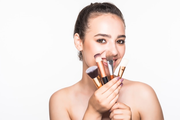 Hermosa mujer con pinceles de maquillaje cerca de su rostro aislado en la pared blanca