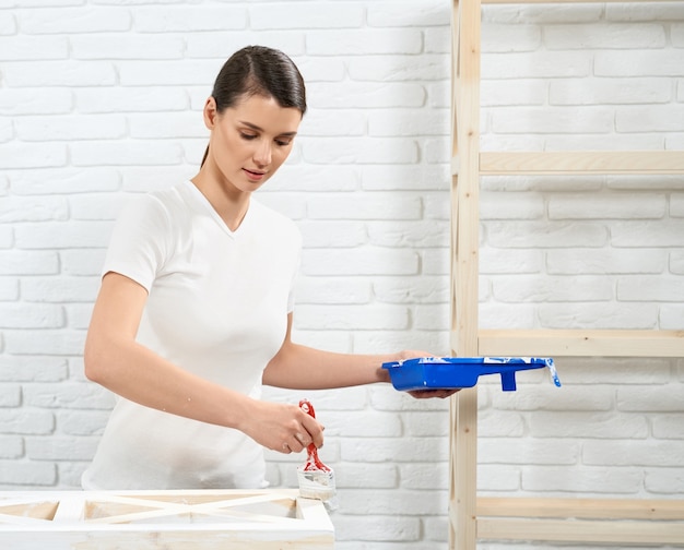 Hermosa mujer pintando muebles antiguos con color blanco