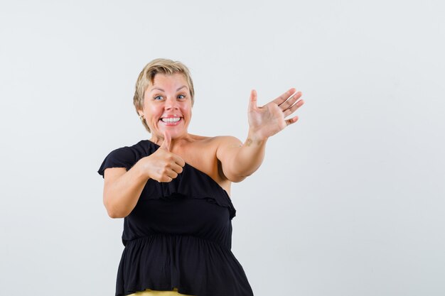 Hermosa mujer posando como mostrando sus notas mientras muestra el pulgar hacia arriba en una blusa negra y se ve alegre.