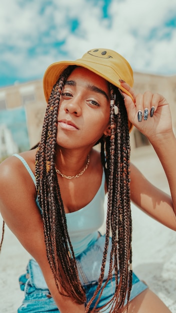 Hermosa mujer con rastas en un sombrero de cubo posando en la cámara