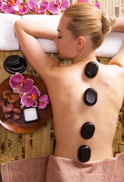 Hermosa mujer relajante en el salón de spa con piedras calientes en el cuerpo. Terapia de tratamientos de belleza