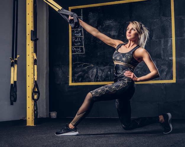 Hermosa mujer en ropa deportiva haciendo ejercicio con sistema de correas de suspensión en el gimnasio.