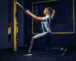 Foto gratuita hermosa mujer en ropa deportiva haciendo ejercicio con sistema de correas de suspensión en el gimnasio.