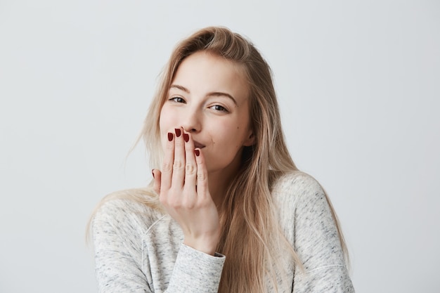 Hermosa mujer rubia de aspecto agradable con manicura roja sopla beso