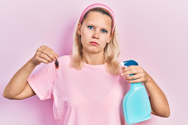 Hermosa mujer rubia caucásica sosteniendo cucarachas y rociadores de pesticidas relajada con expresión seria en la cara. mirada simple y natural a la cámara.