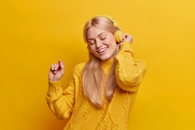 Hermosa mujer rubia despreocupada baila mantiene el brazo levantado se relaja con música agradable de auriculares