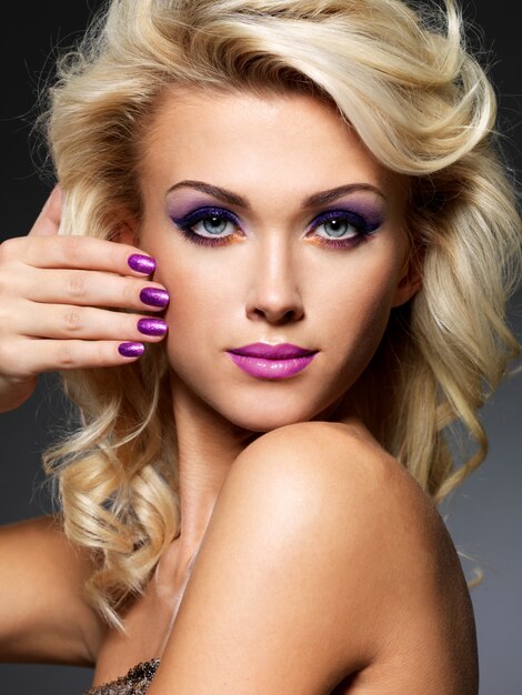 Hermosa mujer rubia con manicura de belleza púrpura y maquillaje de ojos