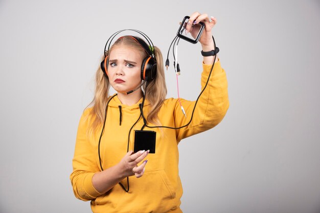 Hermosa mujer rubia mostrando auriculares y con cara de tristeza.