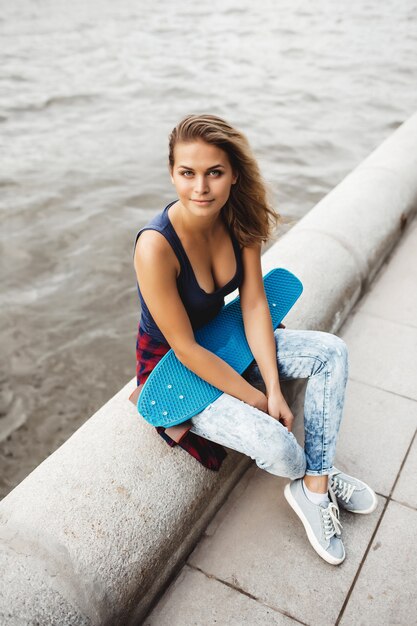 hermosa mujer rubia posando con un monopatín