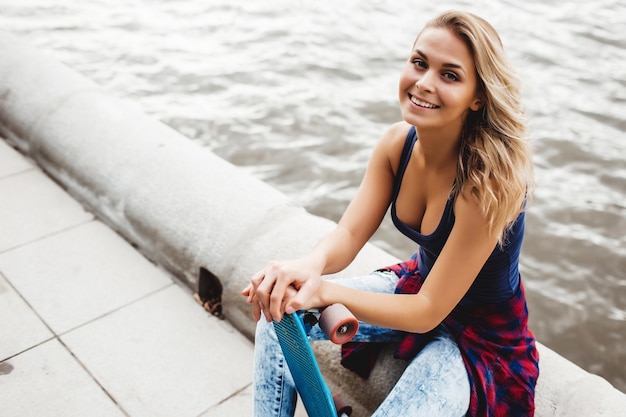 hermosa mujer rubia posando con un monopatín