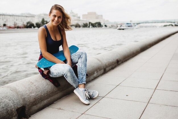 hermosa mujer rubia posando con un monopatín