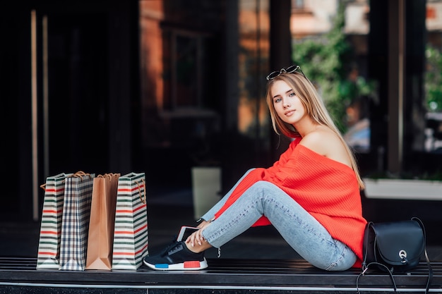 Hermosa mujer rubia sentada en la calle y rodeada de bolsas de la compra.