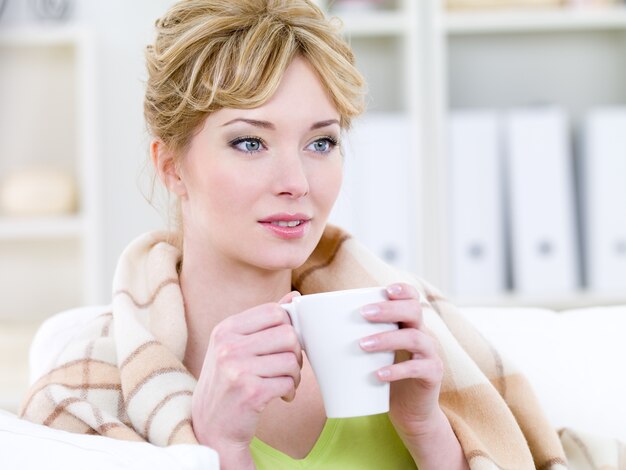 Hermosa mujer rubia con sonrisa fácil bebiendo café caliente - en el interior