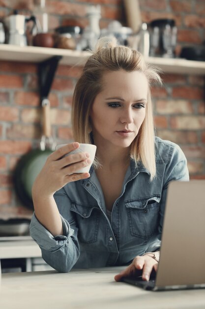 Hermosa mujer rubia con taza de café y portátil