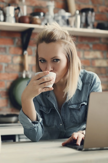 Hermosa mujer rubia con taza de café y portátil