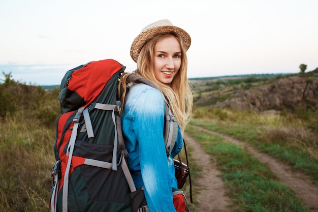 Hermosa mujer rubia viajera con mochila sonriendo, fondo del cañón