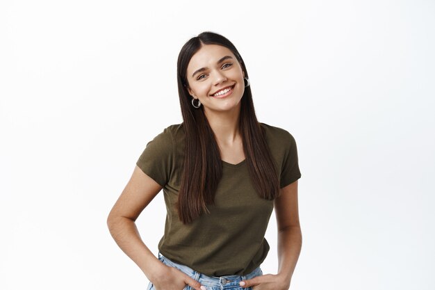 Hermosa mujer sana con sonrisa sincera, de pie relajado contra el fondo blanco, mirando feliz