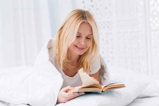 Hermosa mujer senior leyendo un libro en la cama