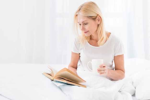 Hermosa mujer senior leyendo un libro mientras toma un café