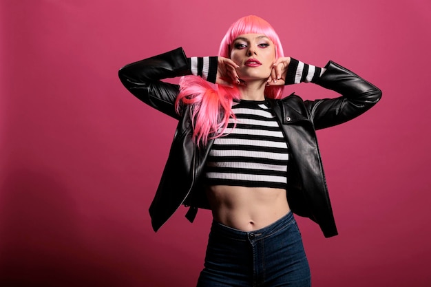 Hermosa mujer sensual con cabello rosado con chaqueta de cuero punk para estar a la moda y anunciar el estilo de la moda rockera. Modelo femenino sintiéndose funky y atractivo, de pie sobre el fondo del estudio.