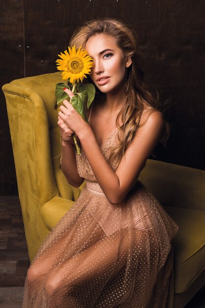 Hermosa mujer sensual sentada en el sillón y posando con girasol