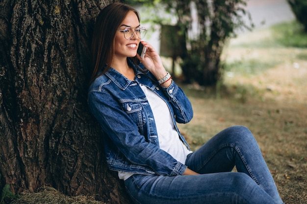 Hermosa mujer sentada bajo un árbol y hablando por teléfono