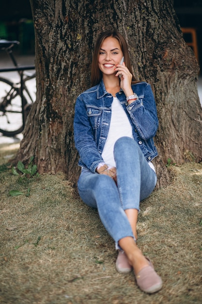 Hermosa mujer sentada bajo un árbol y hablando por teléfono