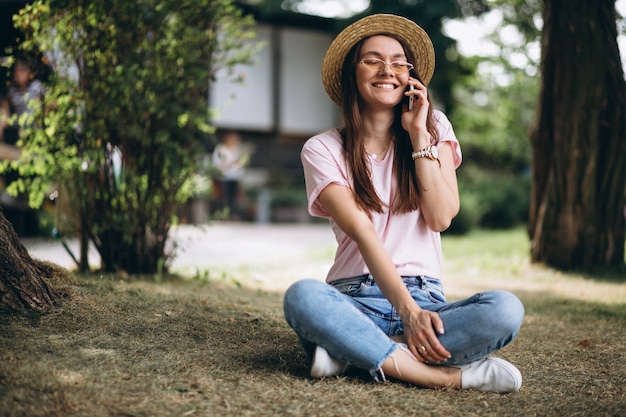 Hermosa mujer sentada bajo un árbol y hablando por teléfono