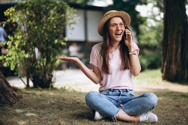 Hermosa mujer sentada bajo un árbol y hablando por teléfono