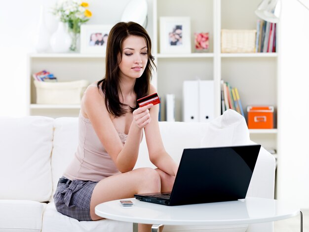 Hermosa mujer sentada en casa y de compras con laptop y tarjeta de crédito