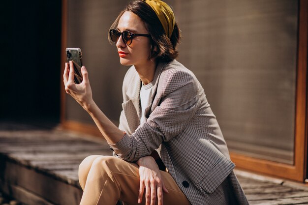 Hermosa mujer sentada en el patio trasero y usando el teléfono