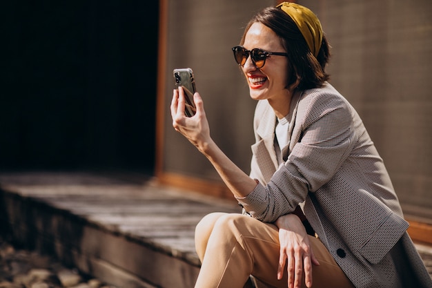 Hermosa mujer sentada en el patio trasero y usando el teléfono