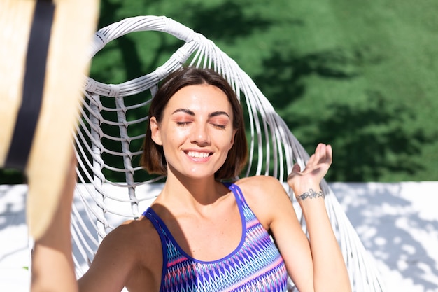 Hermosa mujer sentada en la silla del patio trasero en un día soleado de verano disfrutando de un clima cálido increíble, atrapando los rayos del sol