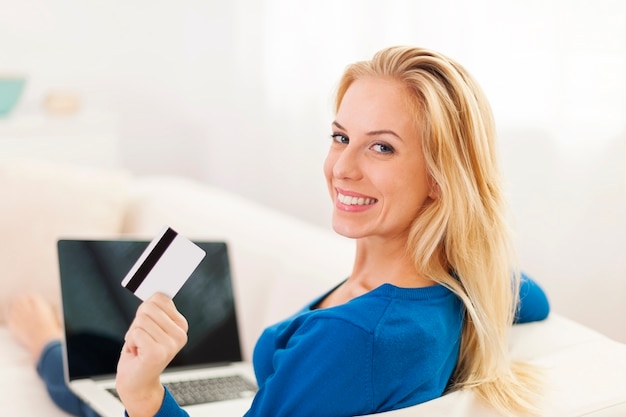 Hermosa mujer sentada en el sofá con laptop y tarjeta de crédito