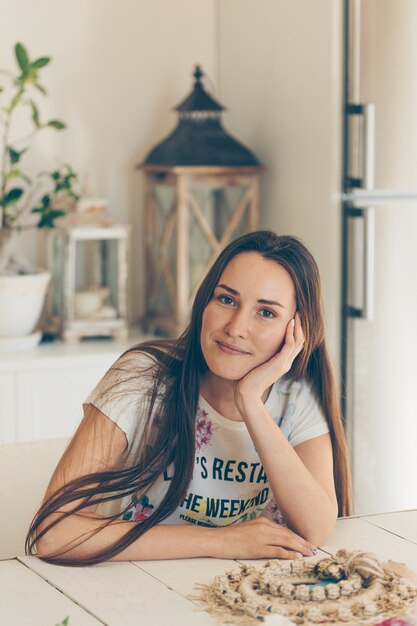 Hermosa mujer sentada y sonriendo en casa en jeans y camiseta durante el día