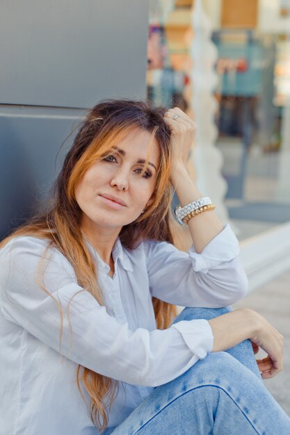 Hermosa mujer sentada en el suelo sonriendo en la calle durante el día y. .