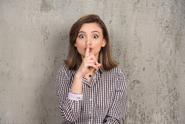 Foto gratuita hermosa mujer seria haciendo el signo de silencio y posando contra la pared gris del estudio