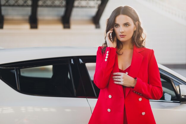 Hermosa mujer sexy en traje rojo posando en el coche hablando de negocios por teléfono